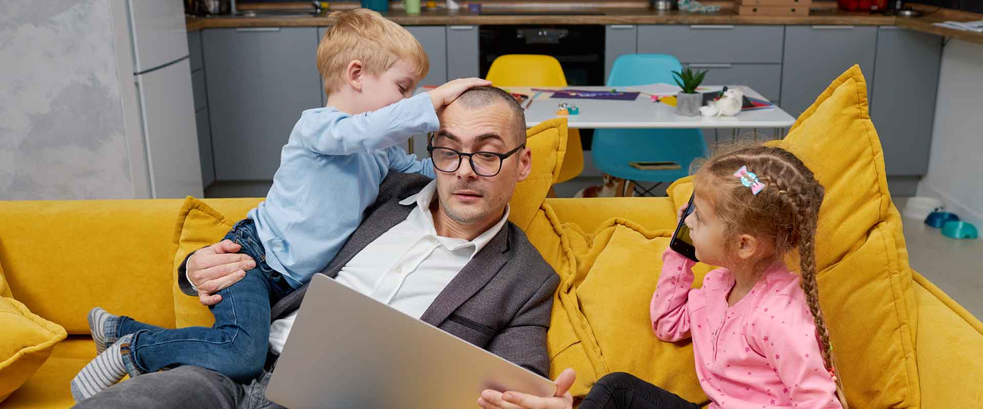 businessman and his small children climbing on him as he works on a laptop computer
