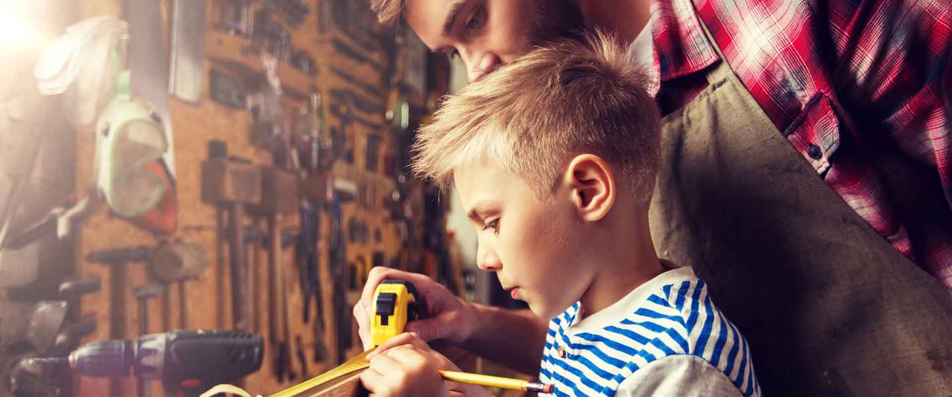 father supervising his young son working on a woodwork table with measuring tape and pencil