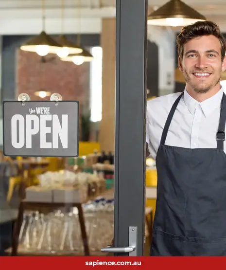 smiling proud business owner standing near an open door with the sign, open for business