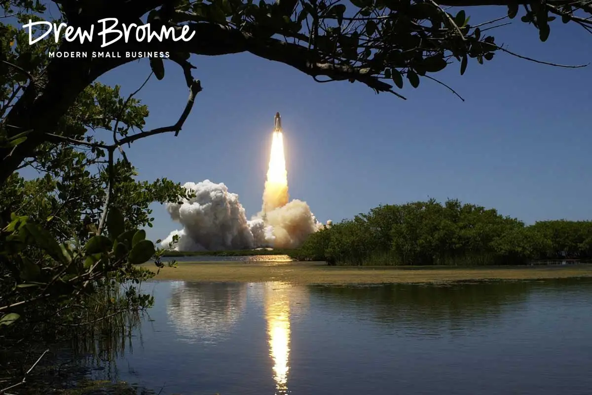 A photo at dusk of the long range launch of a rocket in the distance framed boy overhead trees wall reflected in water below