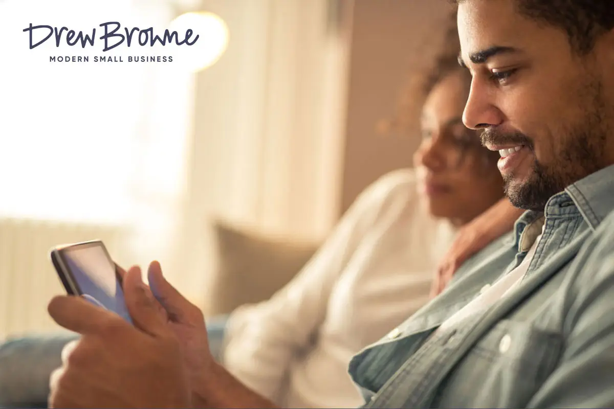 A happy and contented couple sitting on the couch while one of them cheques the mobile device